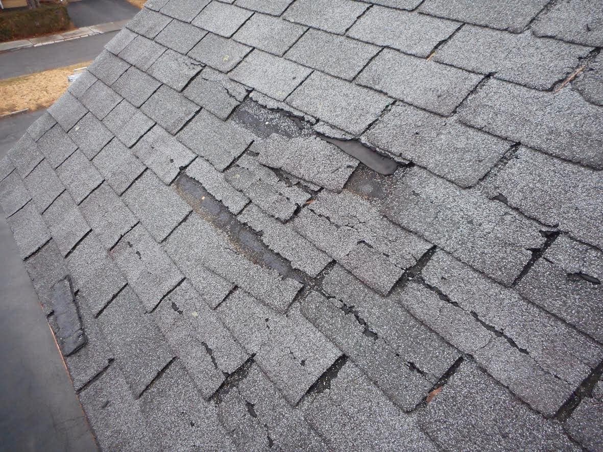 Asphalt shingle roof with torn and missing shingle tabs after a storm